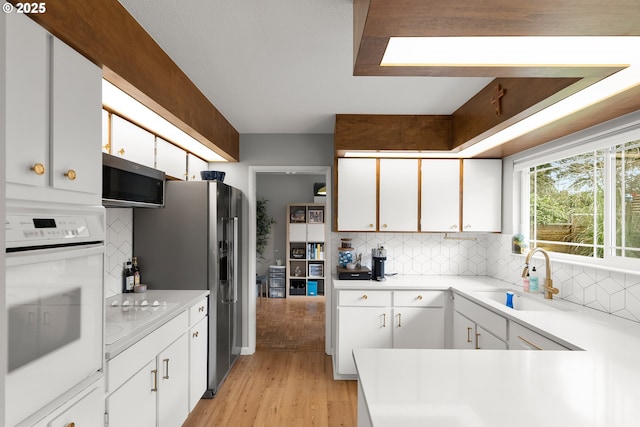 3730 NW 183rd Ave, Portland, OR 97229 - kitchen featuring stainless steel appliances, light wood finished floors, white cabinetry, and decorative backsplash