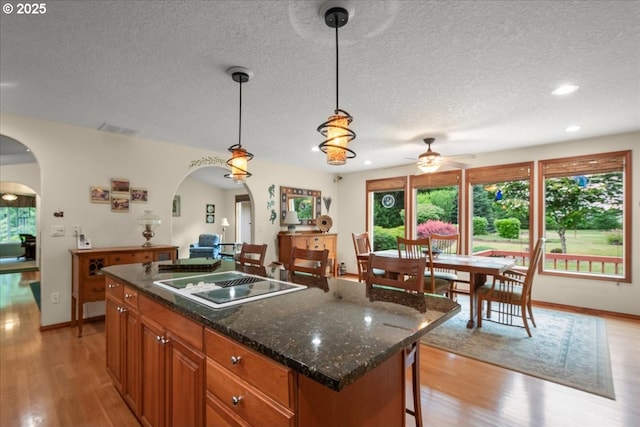 110 Dolph Dr, Ariel, WA 98603 - kitchen featuring stovetop with downdraft, arched walkways, a ceiling fan, brown cabinets, and light wood-style flooring