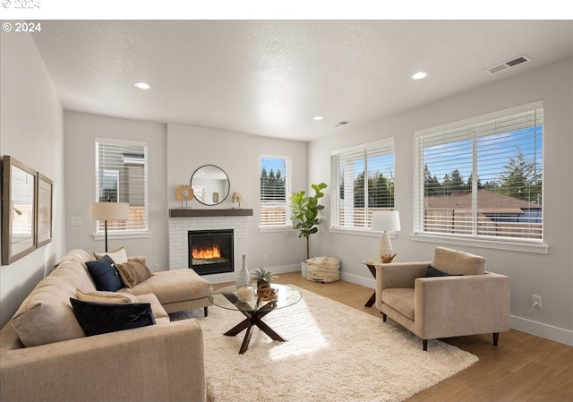 living room featuring wood finished floors, visible vents, baseboards, a fireplace, and a textured ceiling