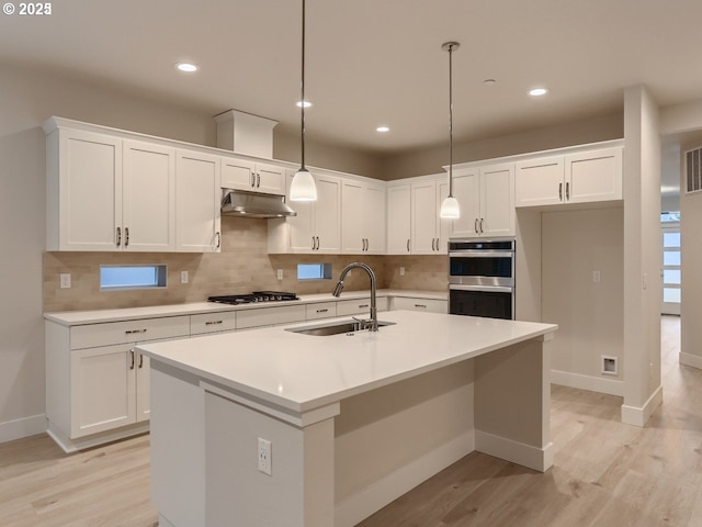 kitchen featuring tasteful backsplash, under cabinet range hood, gas stovetop, white cabinetry, and a sink