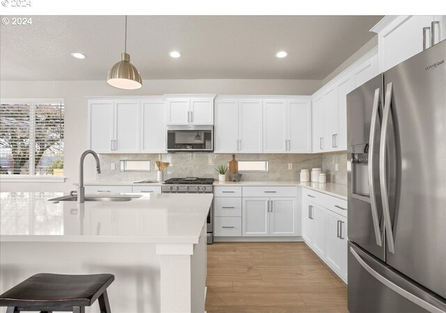 kitchen with light wood-type flooring, a sink, backsplash, stainless steel appliances, and light countertops