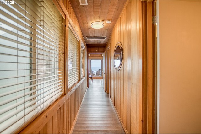 hall featuring light wood-style floors, wood walls, and visible vents