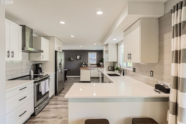 1736 Regency St, West Linn, OR 97068 - kitchen featuring wall chimney range hood, appliances with stainless steel finishes, a peninsula, tasteful backsplash, and light wood-style flooring