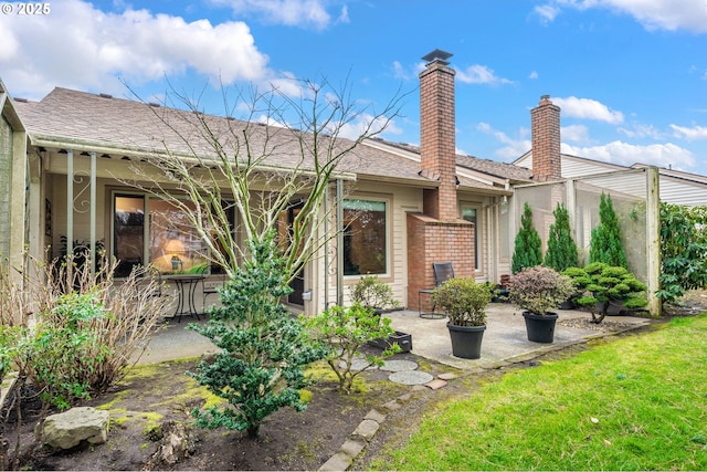 back of property with a chimney, a patio, and roof with shingles