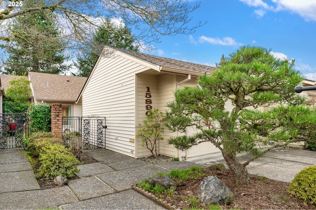 view of property exterior featuring roof with shingles, an attached garage, and fence