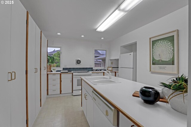 kitchen with light countertops, white cabinetry, a sink, and white appliances