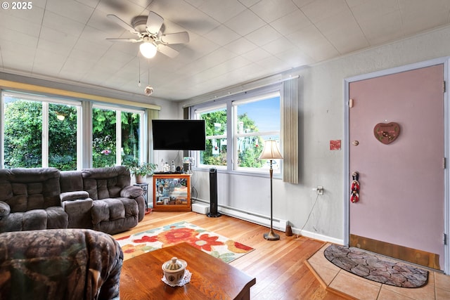 living area featuring light wood-style floors, ceiling fan, a baseboard heating unit, and baseboards