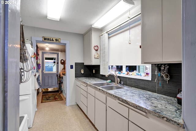 kitchen with tasteful backsplash, white cabinets, light countertops, and a sink