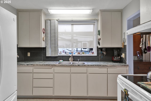 kitchen with light stone counters, white appliances, decorative backsplash, and a sink
