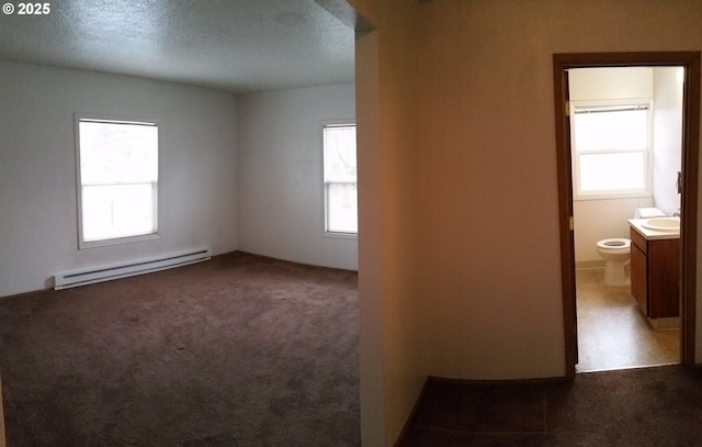 empty room with dark colored carpet, a baseboard radiator, sink, and a textured ceiling