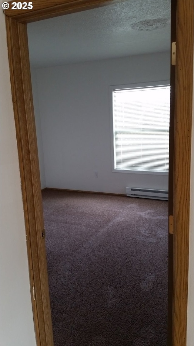 carpeted spare room with a baseboard heating unit and a textured ceiling