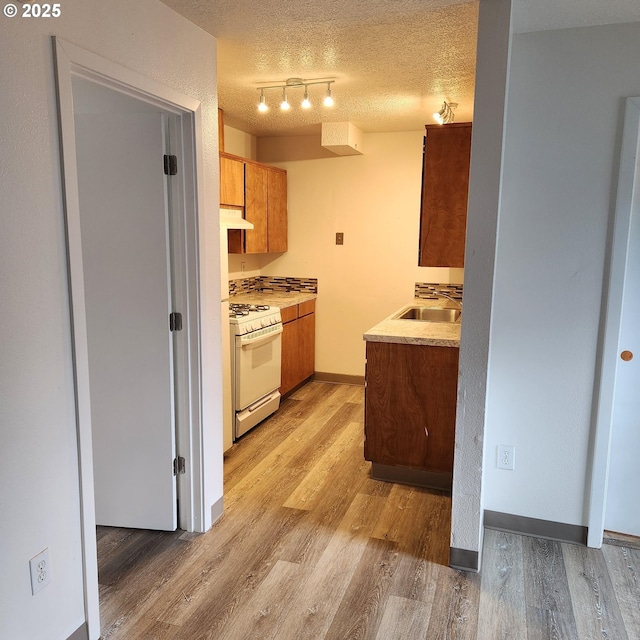 kitchen featuring sink, a textured ceiling, light hardwood / wood-style flooring, track lighting, and white range with gas cooktop