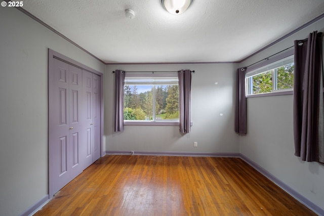 unfurnished bedroom with hardwood / wood-style floors, a closet, baseboards, and crown molding
