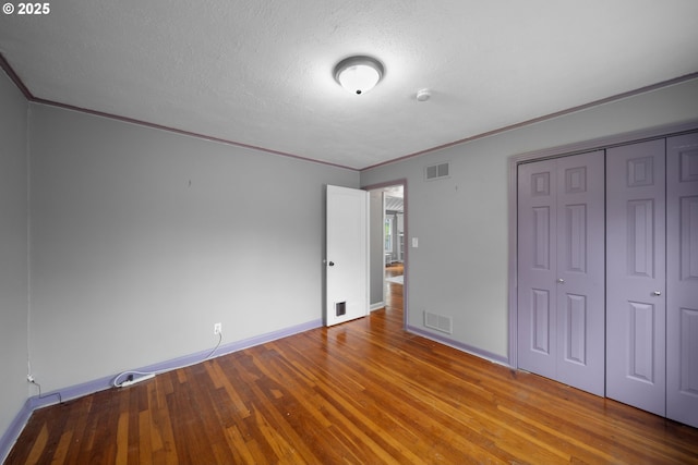 unfurnished bedroom featuring crown molding, wood finished floors, baseboards, a textured ceiling, and a closet
