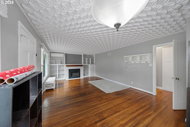 unfurnished living room with wood finished floors, built in shelves, baseboards, a fireplace, and an ornate ceiling