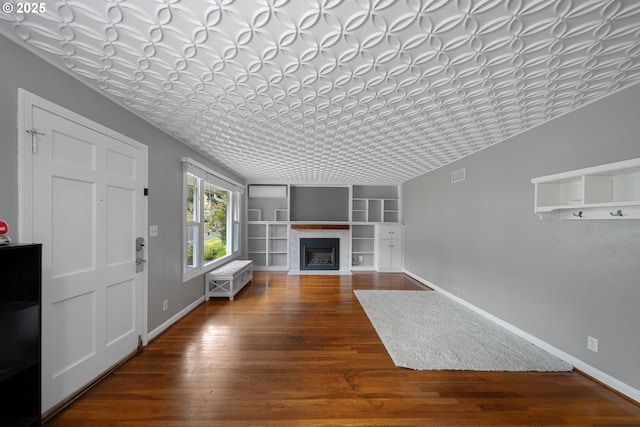 unfurnished living room with hardwood / wood-style floors, a fireplace with flush hearth, baseboards, and built in features