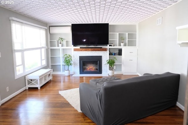 living room featuring a fireplace with flush hearth, built in features, and wood finished floors