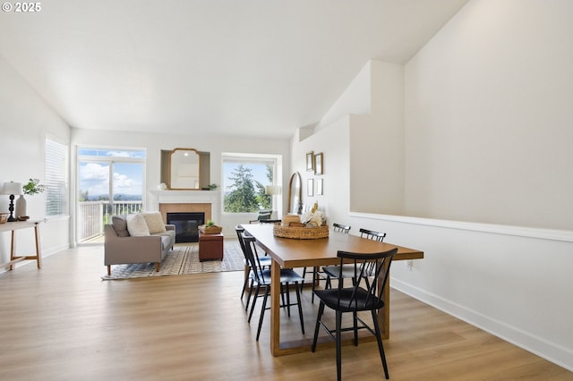 dining space featuring healthy amount of natural light, a glass covered fireplace, baseboards, and light wood finished floors