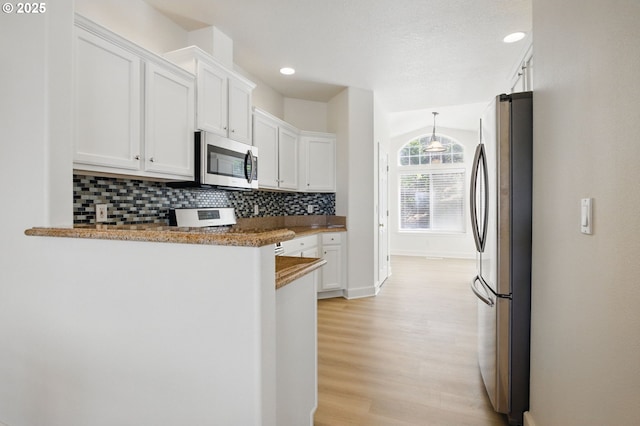 kitchen featuring appliances with stainless steel finishes, white cabinetry, backsplash, light wood finished floors, and a peninsula