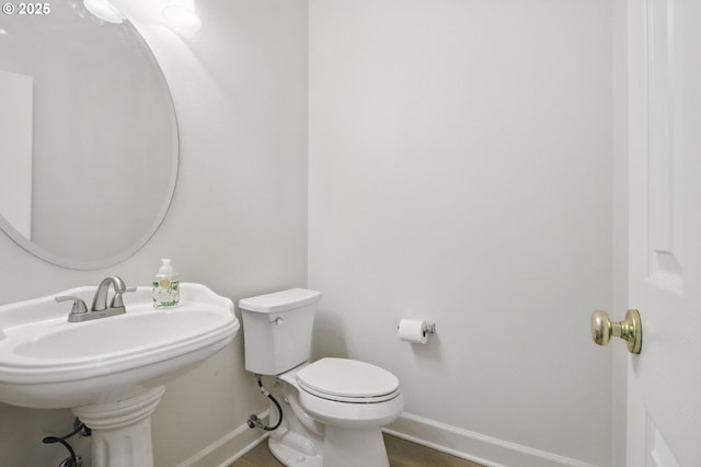 half bathroom with baseboards, toilet, a sink, and wood finished floors