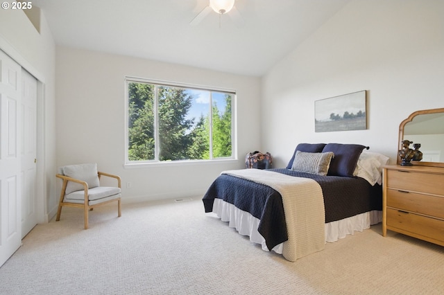 bedroom with vaulted ceiling, light colored carpet, a closet, and a ceiling fan