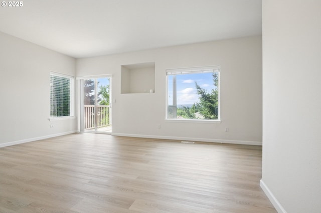 empty room with plenty of natural light, light wood-style floors, and baseboards