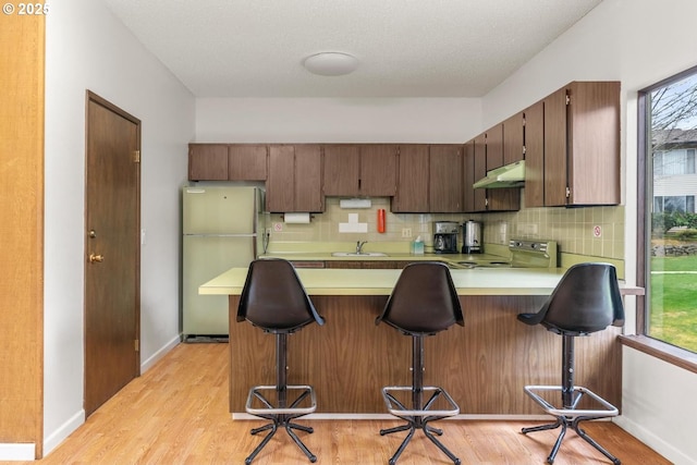 kitchen featuring a breakfast bar area, refrigerator, electric range, kitchen peninsula, and decorative backsplash