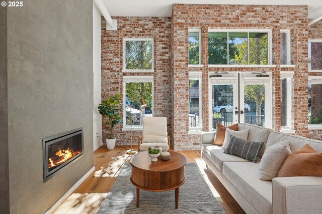 109 SW Gibbs St, Portland, OR 97239 - living area featuring a glass covered fireplace, wood finished floors, brick wall, a towering ceiling, and french doors