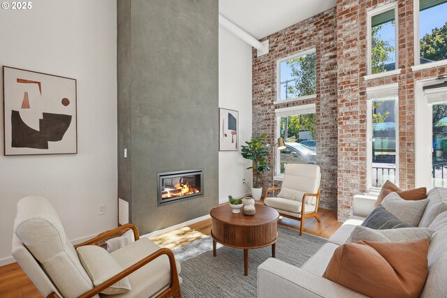 109 SW Gibbs St, Portland, OR 97239 - living room with a high ceiling, wood finished floors, a glass covered fireplace, baseboards, and brick wall