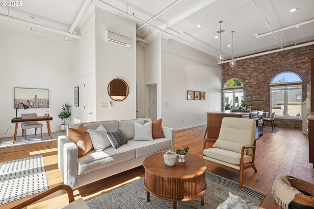 109 SW Gibbs St, Portland, OR 97239 - living room featuring a towering ceiling, light wood-type flooring, brick wall, baseboards, and an AC wall unit