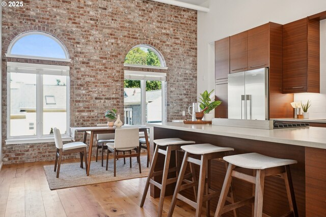 109 SW Gibbs St, Portland, OR 97239 - kitchen featuring high quality fridge, brick wall, a high ceiling, a breakfast bar area, and light wood-type flooring