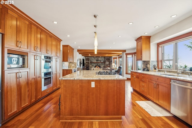 kitchen with appliances with stainless steel finishes, pendant lighting, wood-type flooring, a center island, and light stone counters