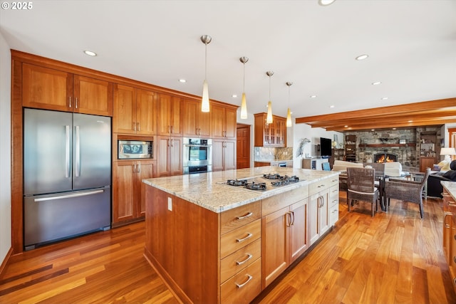 kitchen with light hardwood / wood-style flooring, appliances with stainless steel finishes, a fireplace, a kitchen island, and decorative light fixtures