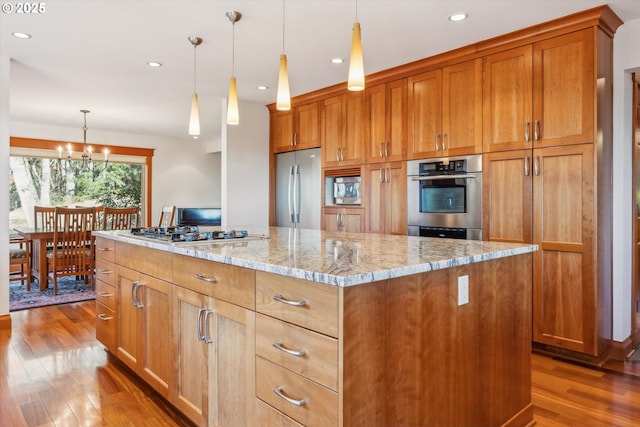 kitchen with light stone counters, wood-type flooring, decorative light fixtures, appliances with stainless steel finishes, and a kitchen island