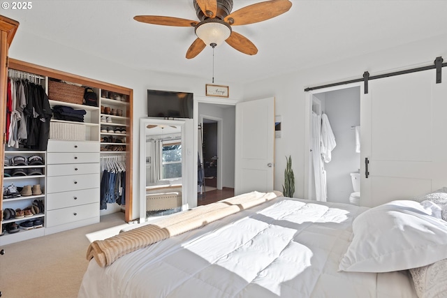 carpeted bedroom featuring connected bathroom, a closet, a barn door, and ceiling fan