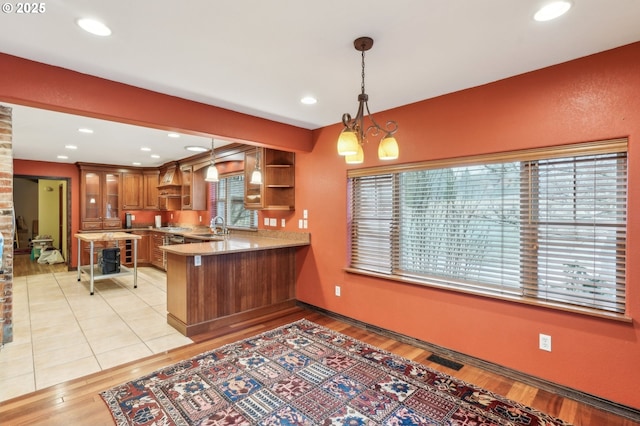 kitchen featuring light wood-type flooring, kitchen peninsula, pendant lighting, sink, and an inviting chandelier