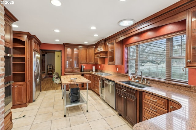 kitchen with custom exhaust hood, appliances with stainless steel finishes, light stone countertops, light tile patterned floors, and sink