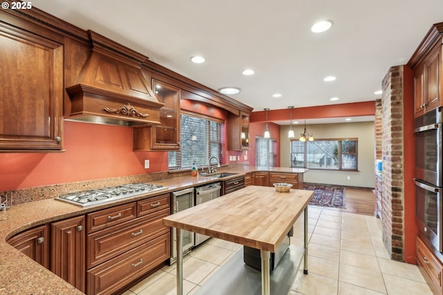 kitchen with light stone counters, premium range hood, decorative light fixtures, stainless steel appliances, and sink