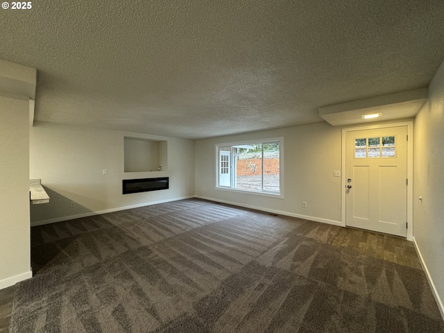 unfurnished living room with a textured ceiling, dark carpet, a glass covered fireplace, and baseboards