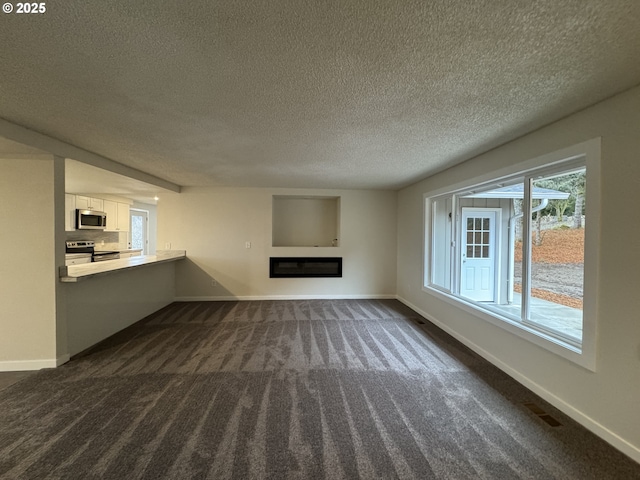 unfurnished living room with baseboards, dark colored carpet, a textured ceiling, and a glass covered fireplace