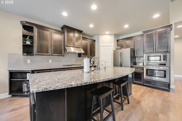 kitchen featuring decorative backsplash, light wood-type flooring, stainless steel appliances, and a kitchen island with sink