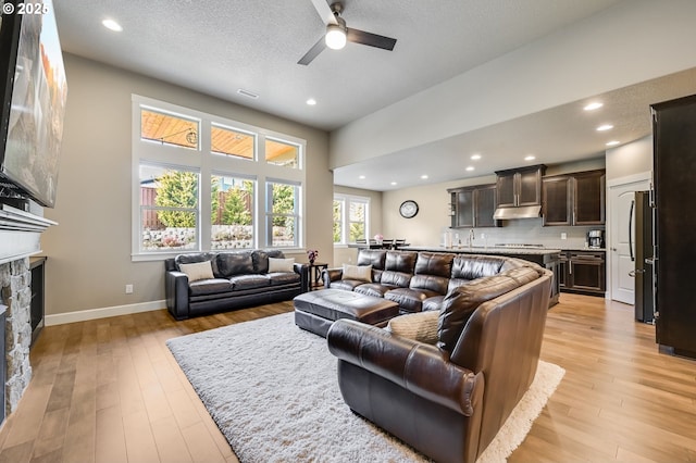 living room with sink, light hardwood / wood-style flooring, a stone fireplace, and a textured ceiling