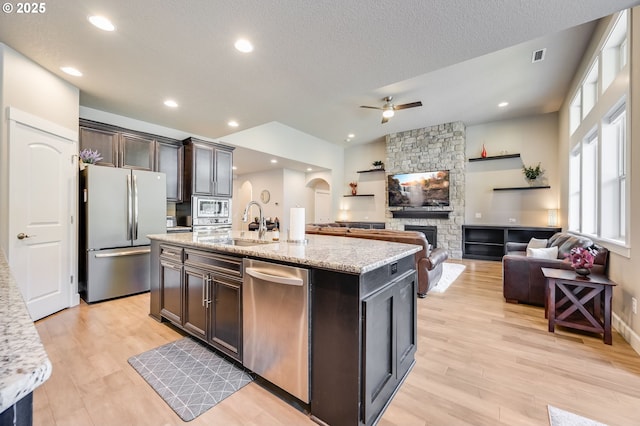 kitchen with an island with sink, light hardwood / wood-style flooring, light stone countertops, dark brown cabinets, and appliances with stainless steel finishes