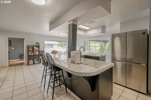 kitchen with tile countertops, freestanding refrigerator, light tile patterned floors, a breakfast bar, and a textured ceiling