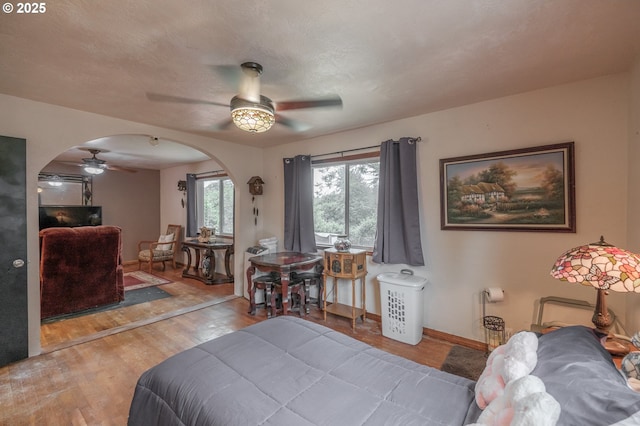 bedroom featuring arched walkways, wood finished floors, baseboards, and a ceiling fan
