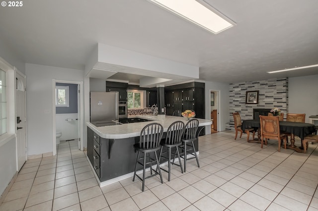 kitchen featuring appliances with stainless steel finishes, a kitchen breakfast bar, light tile patterned floors, light countertops, and a peninsula