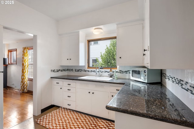 kitchen with tasteful backsplash, stainless steel microwave, a sink, and white cabinets