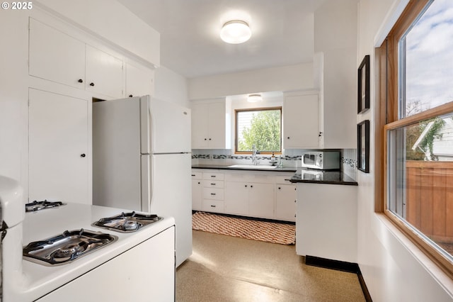 kitchen featuring white appliances, dark countertops, a sink, and white cabinetry