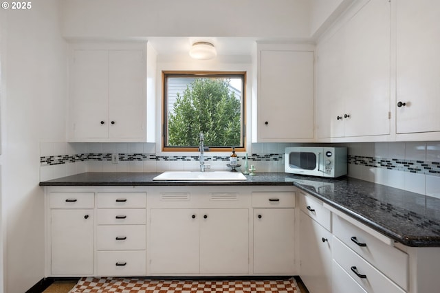 kitchen featuring white microwave, a sink, white cabinets, and tasteful backsplash