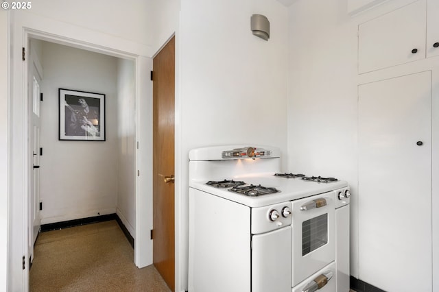 kitchen featuring white range with gas stovetop, white cabinets, light countertops, and baseboards